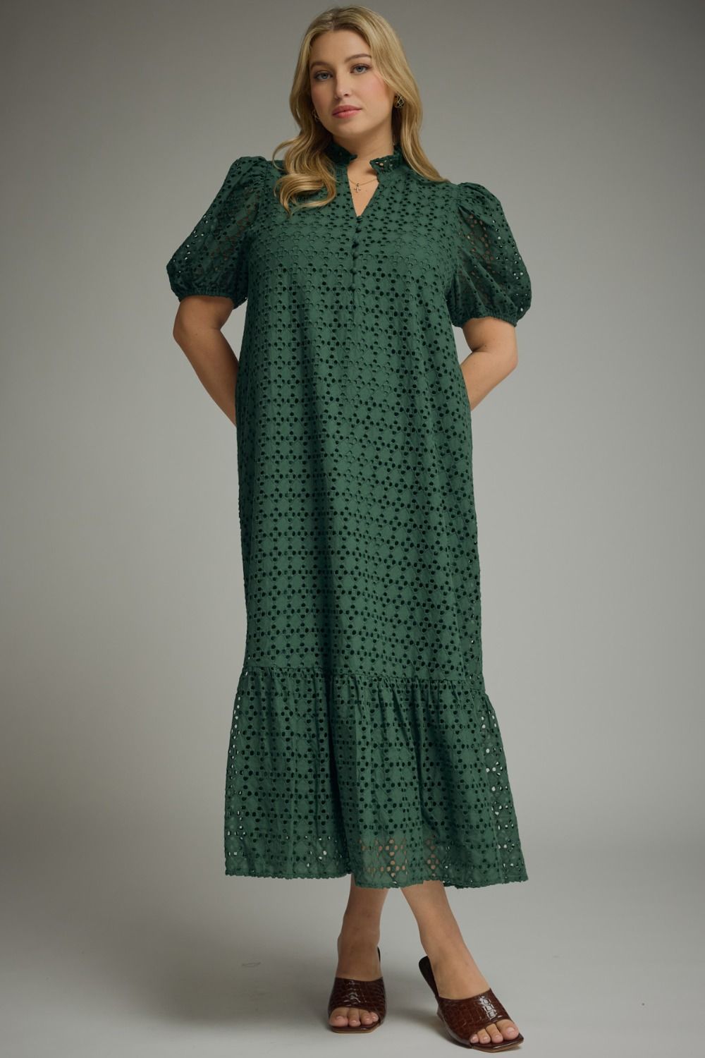Woman wearing an Entro hunter green eyelet midi dress with puff sleeves, ruffled mock neckline, button front, ruffle hem, and side pockets.