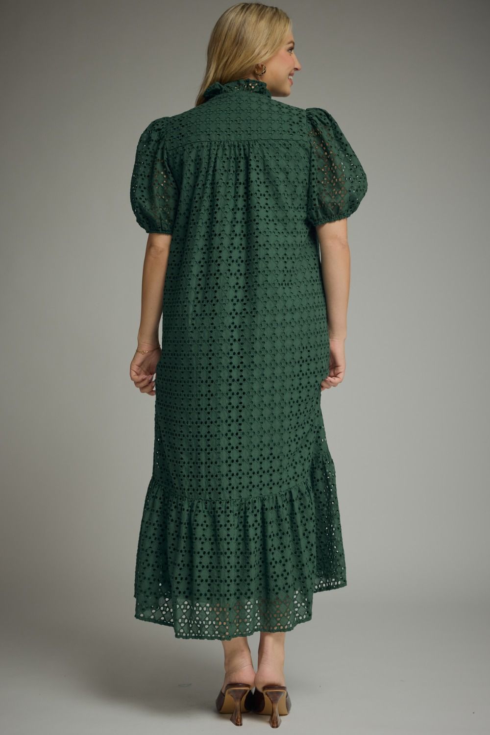 Woman wearing an Entro hunter green eyelet midi dress with puff sleeves, ruffled mock neckline, button front, ruffle hem, and side pockets.