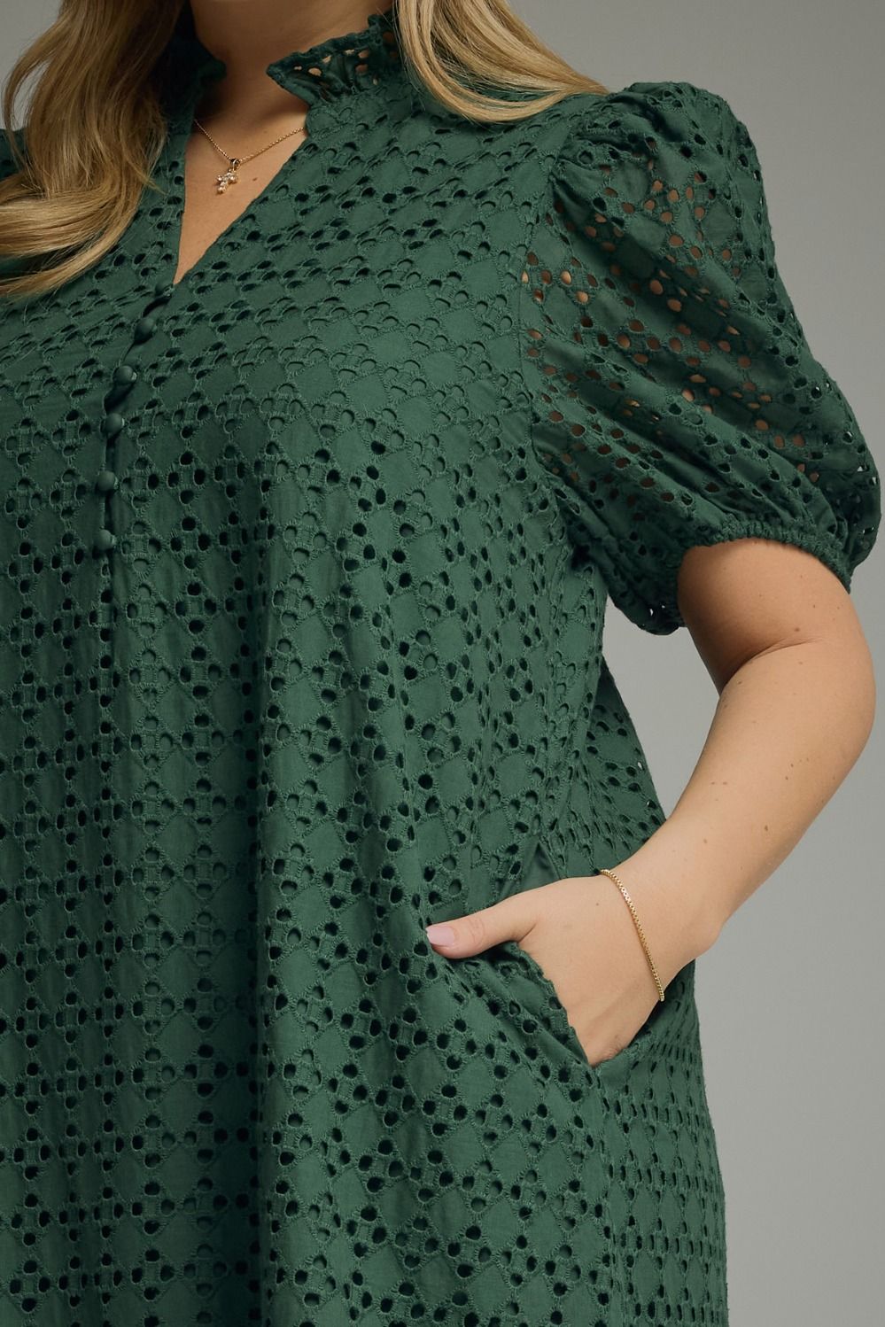 Woman wearing an Entro hunter green eyelet midi dress with puff sleeves, ruffled mock neckline, button front, ruffle hem, and side pockets.