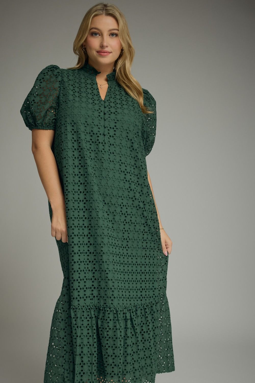Woman wearing an Entro hunter green eyelet midi dress with puff sleeves, ruffled mock neckline, button front, ruffle hem, and side pockets.